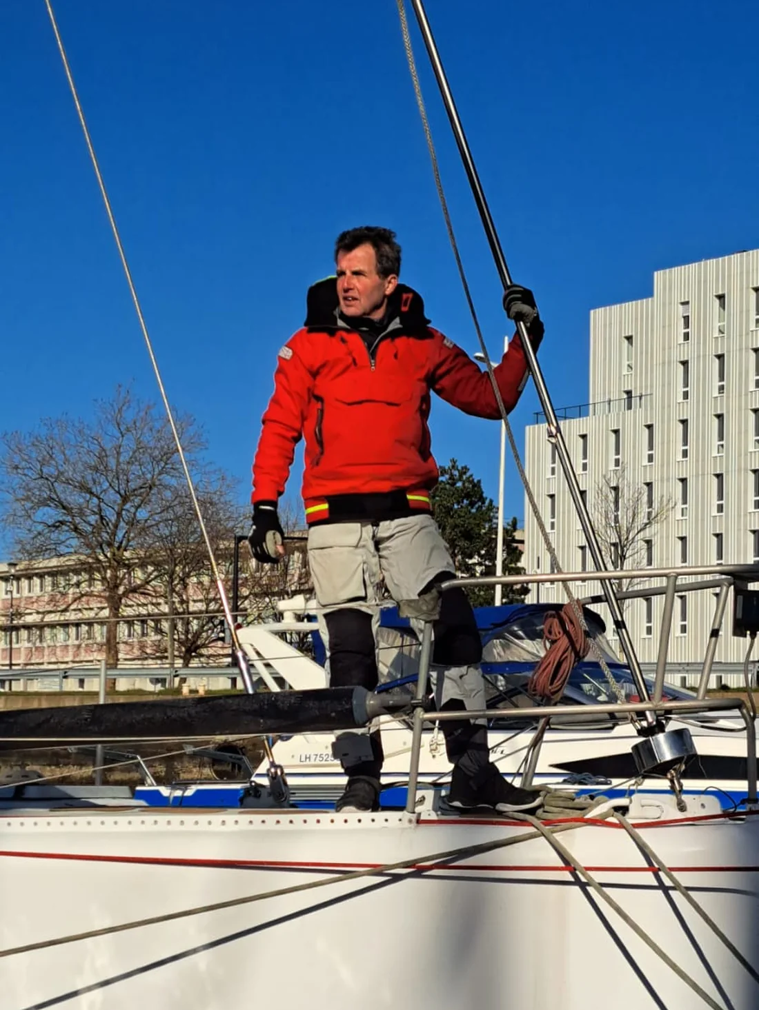Amaury debout sur le pont avant de Tagaroa, la main au gréement, sous un ciel d’hiver bleu