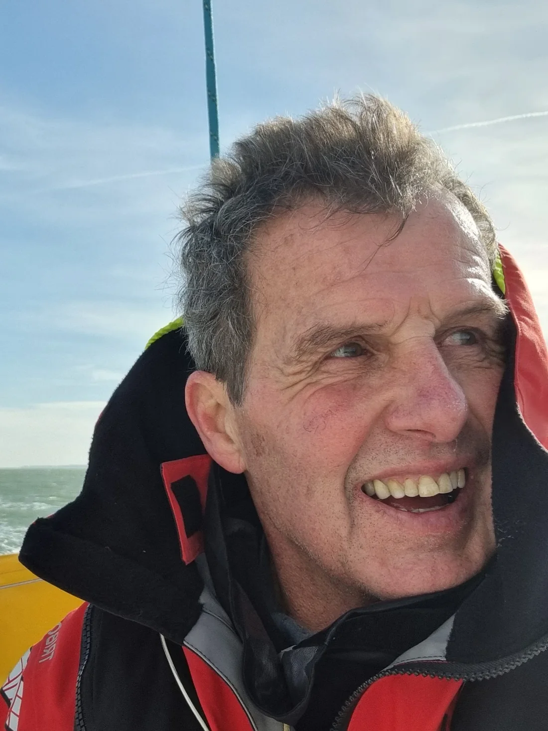 Amaury en mer, cheveux mouillés, souriant dans sa veste de quart rouge