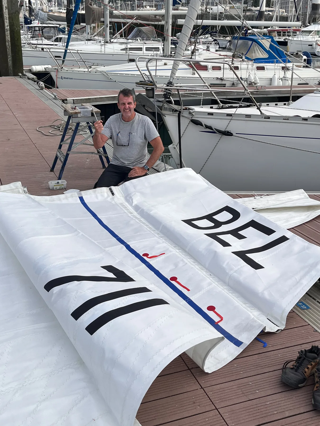 Amaury près de la grand-voile étalée sur le ponton, avec les chiffres BEL 711 fraîchement posés