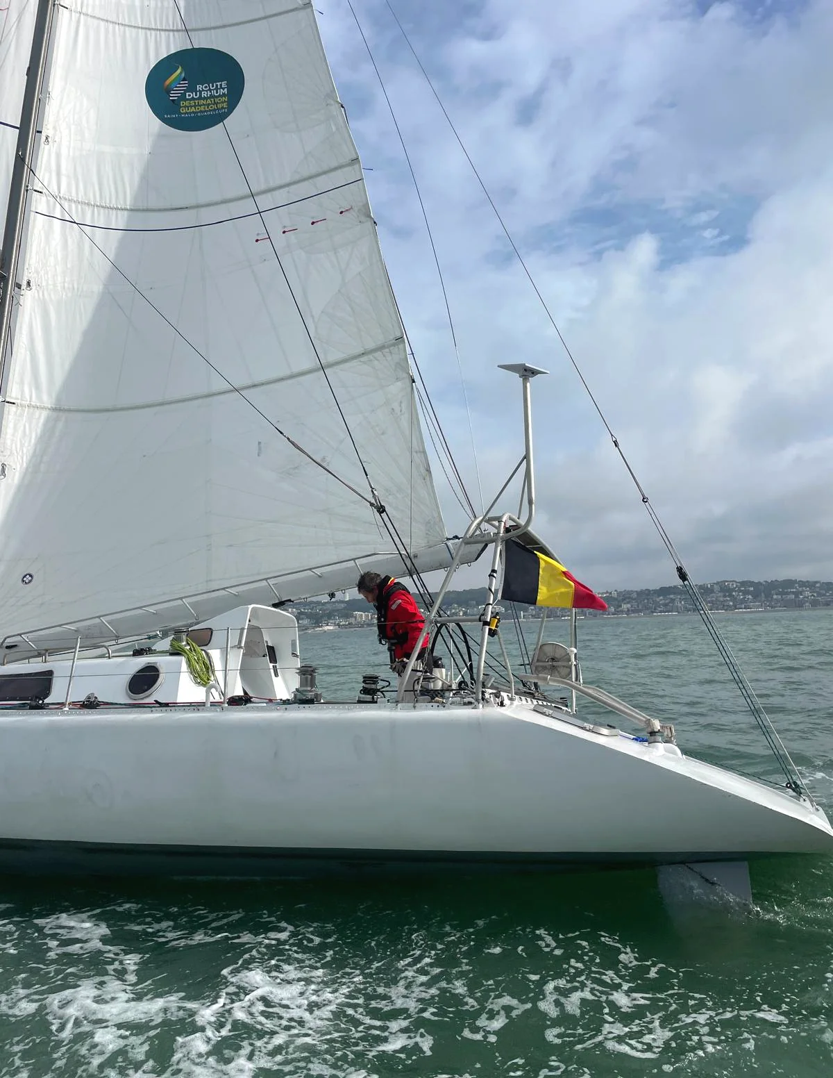 Amaury travaille sur le pont sous le drapeau belge, l’autocollant de la Route du Rhum sur la voile
