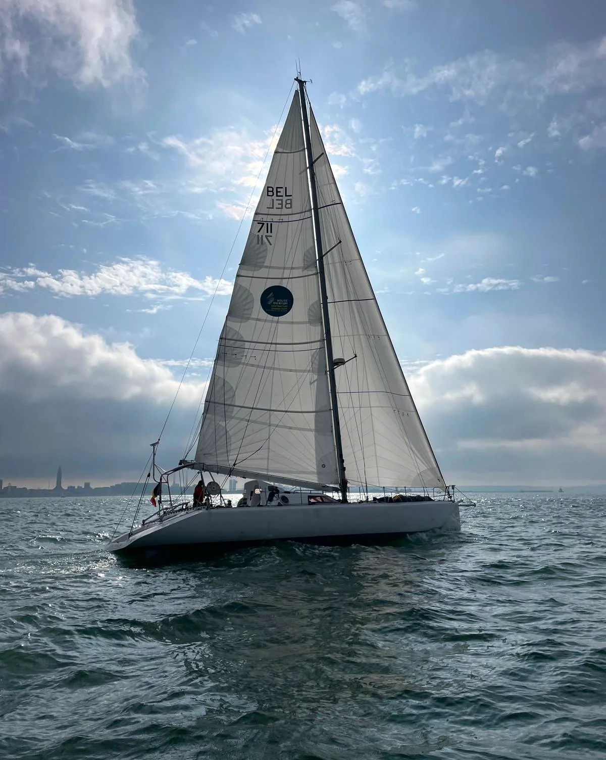 Tagaroa sous grand-voile et génois, la ligne de côte derrière
