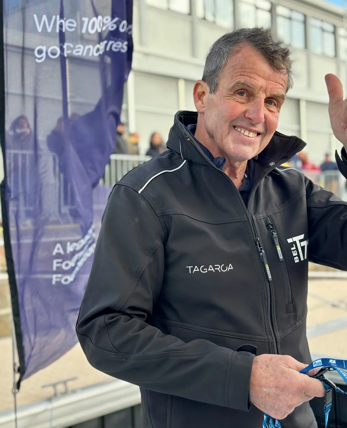 Amaury fait signe depuis le ponton à Saint-Malo, devant la bannière d’Up Against Cancer