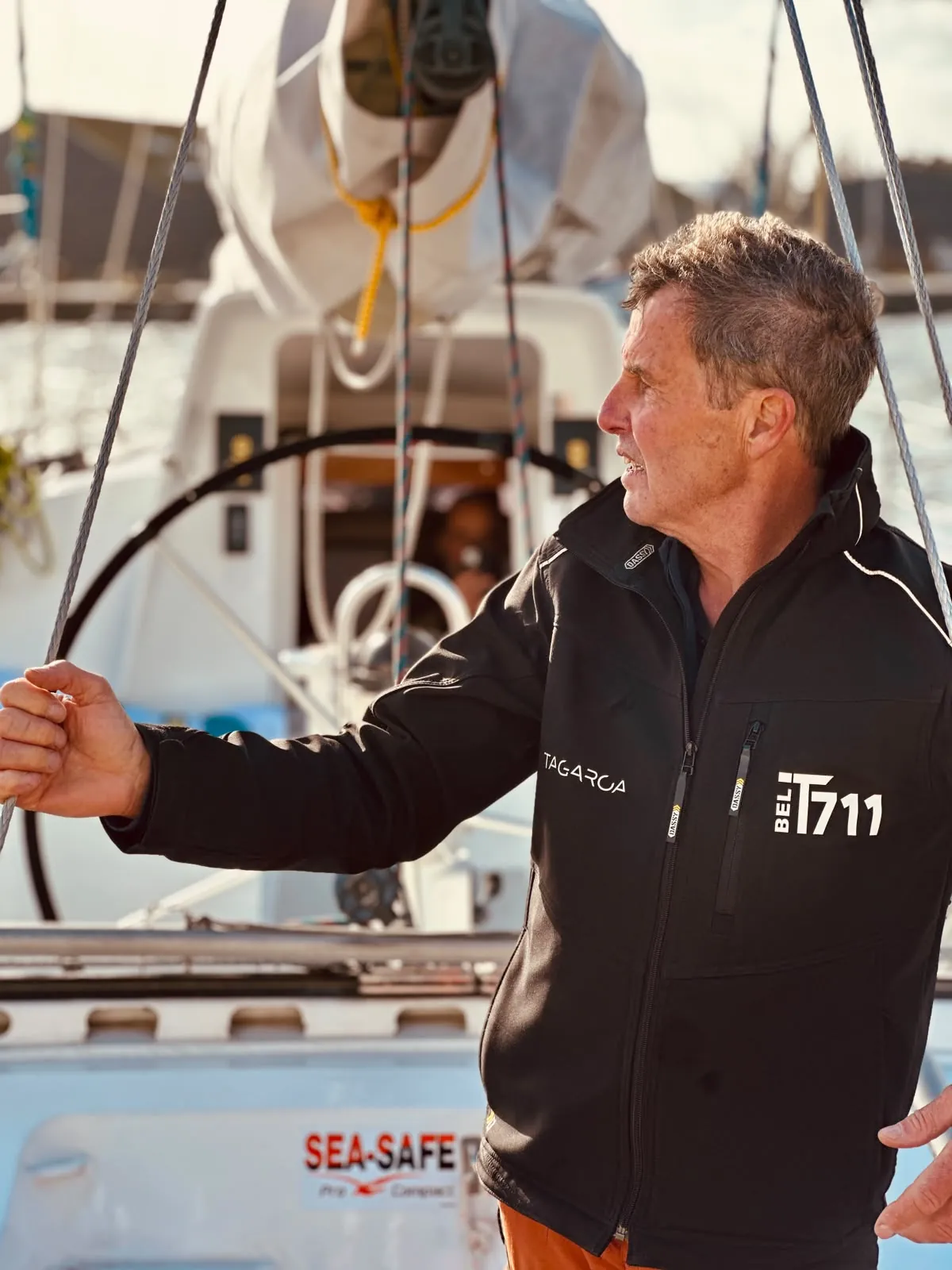 Amaury dans sa veste Tagaroa avec le numéro de voile BEL 711, la main sur le hauban