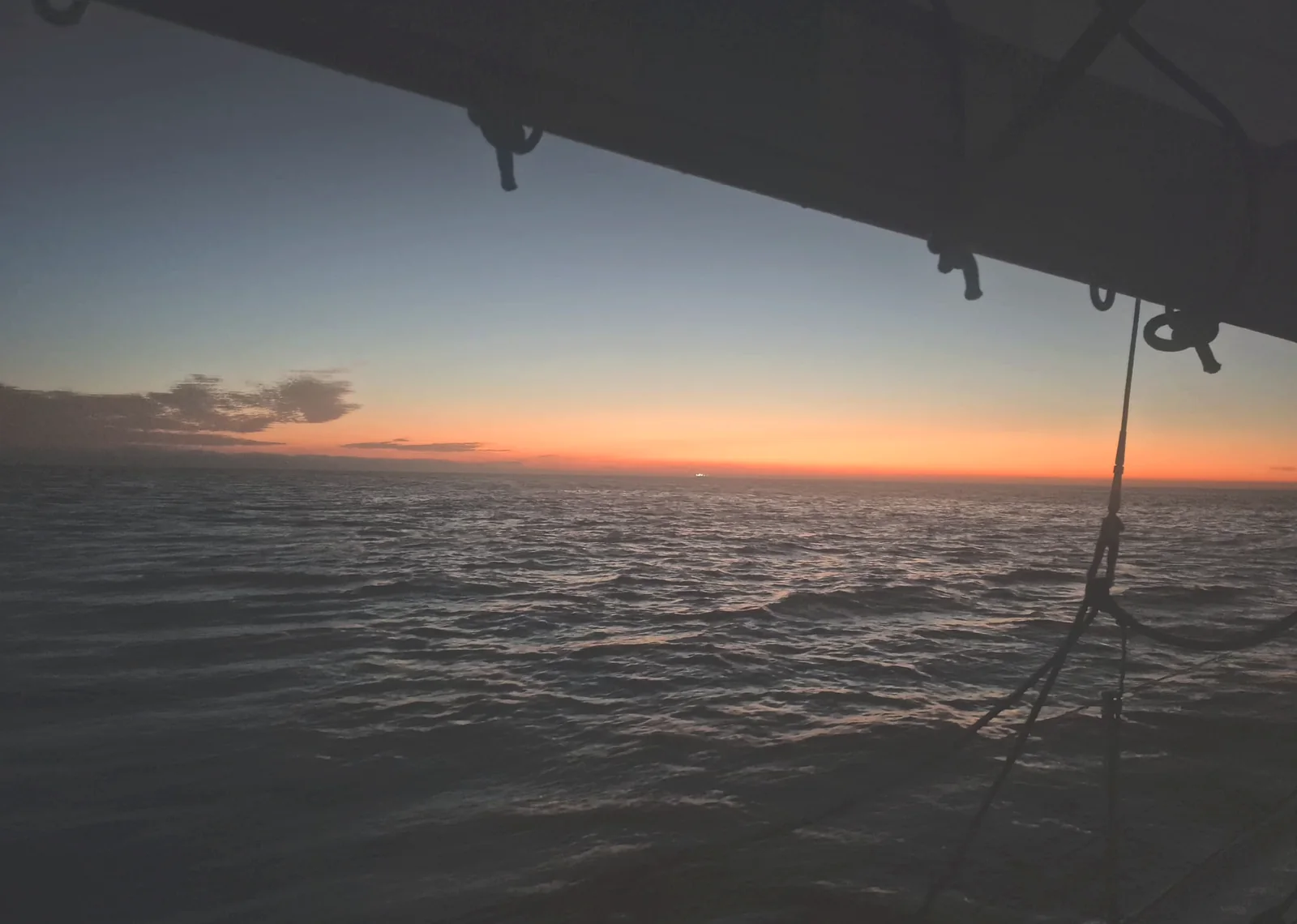 Crépuscule en mer, la bôme noire devant une bande orange à l’horizon